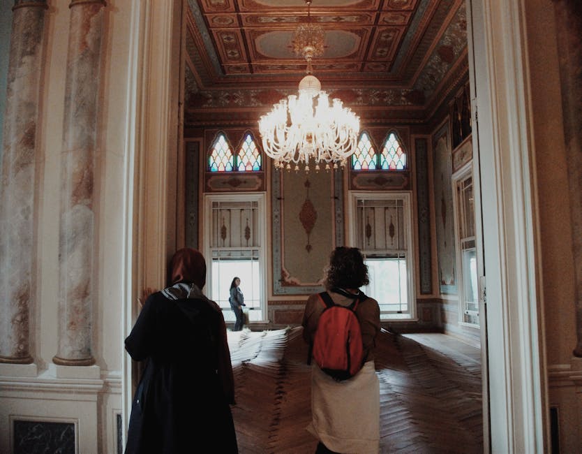 Visitors explore an ornate art museum hall with a stunning chandelier and detailed parquet flooring.